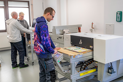 Vordergrund Mann an UV-Drucker, Hintergrund 2 Personen Vordergrund Mann an UV-Drucker, Hintergrund 2 Personen