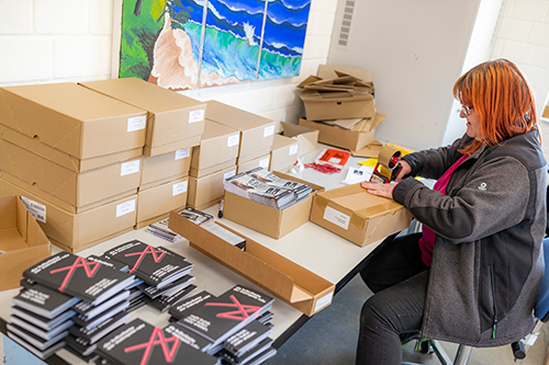 Frau im Lettershop klebt Versandkarton zu